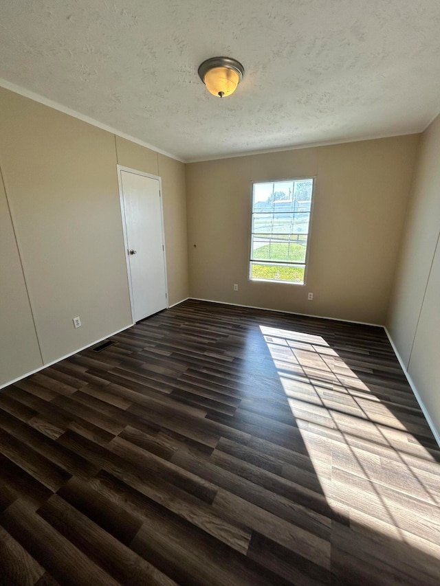 empty room with dark wood-type flooring, crown molding, and a textured ceiling