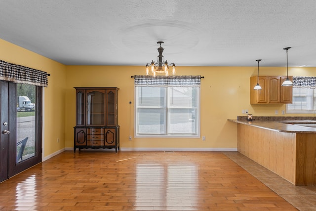 unfurnished dining area featuring an inviting chandelier, a textured ceiling, and light hardwood / wood-style floors