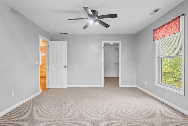 unfurnished bedroom with a closet, a spacious closet, light colored carpet, and ceiling fan