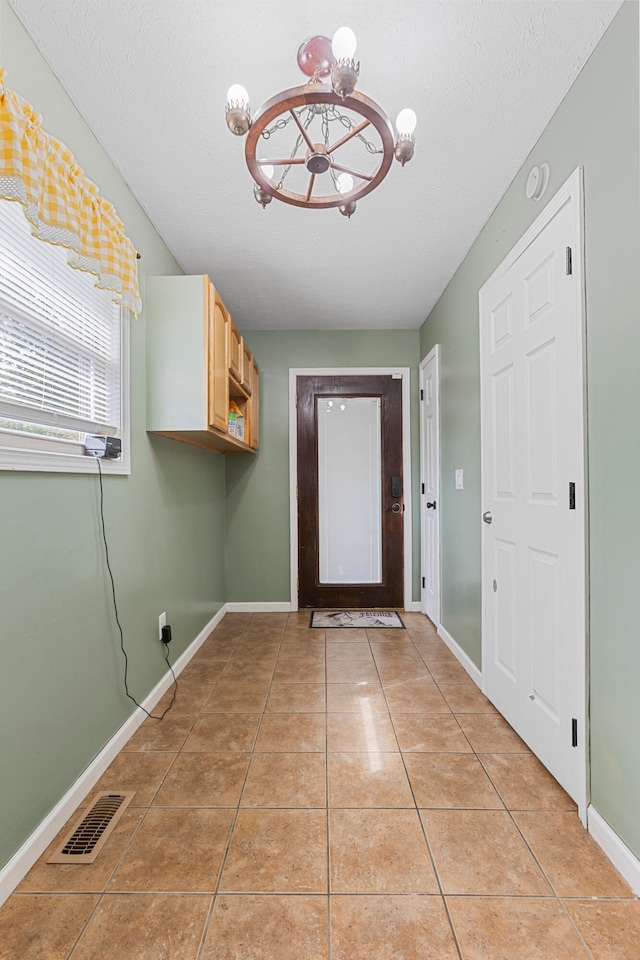 entryway featuring light tile patterned flooring, a textured ceiling, and a chandelier