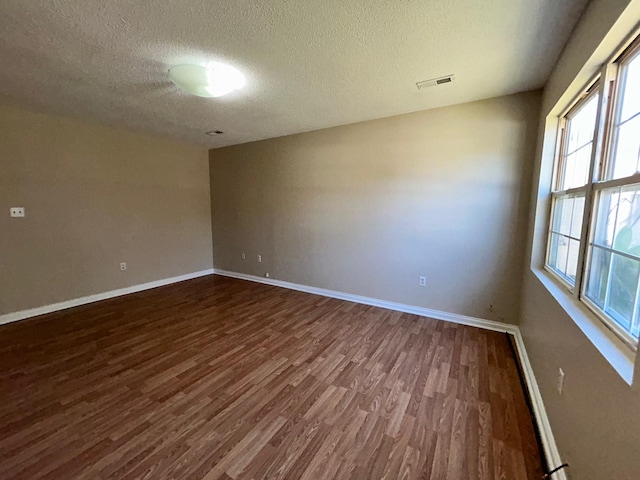 spare room with a textured ceiling and dark hardwood / wood-style floors