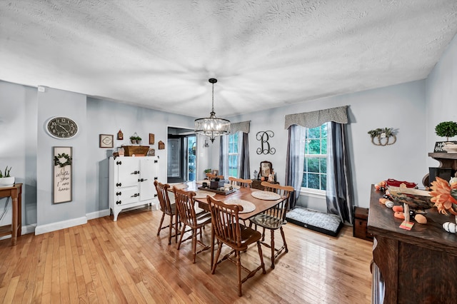 dining space with an inviting chandelier, light wood-type flooring, and a textured ceiling