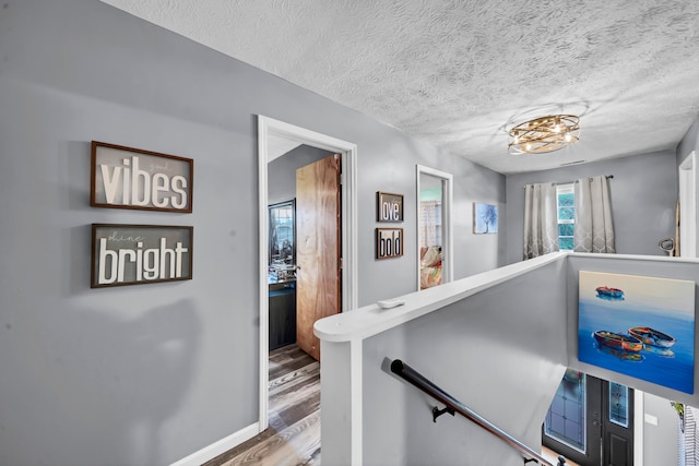 hall featuring hardwood / wood-style flooring, a notable chandelier, and a textured ceiling