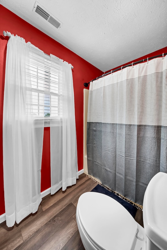 bathroom featuring a textured ceiling, hardwood / wood-style flooring, curtained shower, and toilet