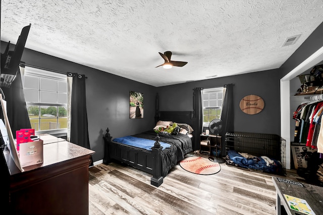 bedroom featuring ceiling fan, a textured ceiling, light hardwood / wood-style flooring, and multiple windows