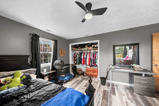 bedroom with multiple windows, light wood-type flooring, ceiling fan, and a closet