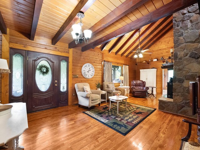 living room featuring ceiling fan with notable chandelier, wooden walls, hardwood / wood-style floors, and beamed ceiling