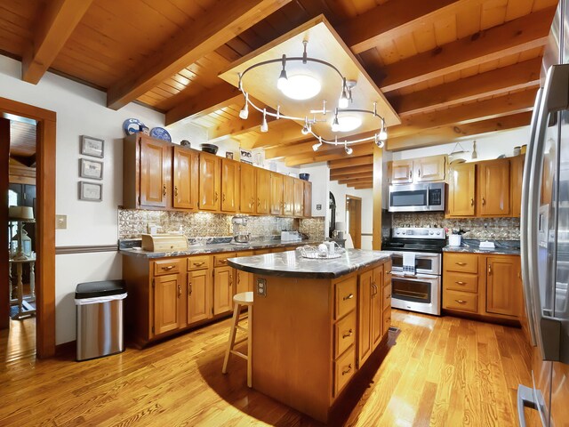 kitchen featuring tasteful backsplash, decorative light fixtures, stainless steel appliances, a center island, and light wood-type flooring