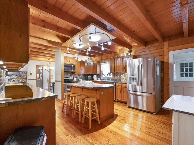 kitchen featuring light hardwood / wood-style floors, beamed ceiling, a center island, a breakfast bar area, and appliances with stainless steel finishes