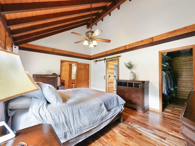 bedroom featuring lofted ceiling with beams, light hardwood / wood-style floors, ceiling fan, and a barn door