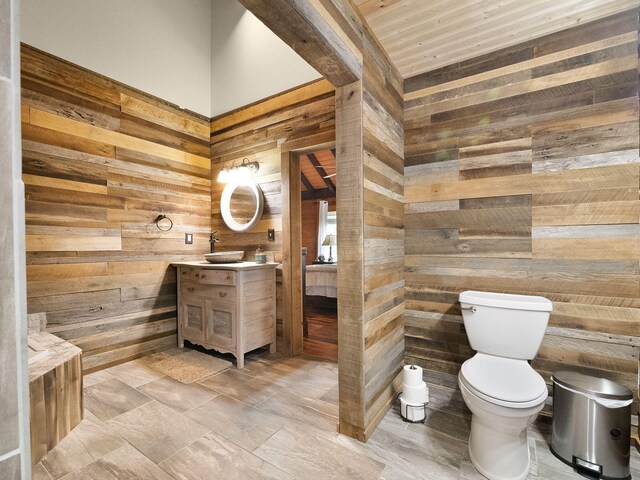 bathroom featuring wooden walls, wood ceiling, vanity, and toilet