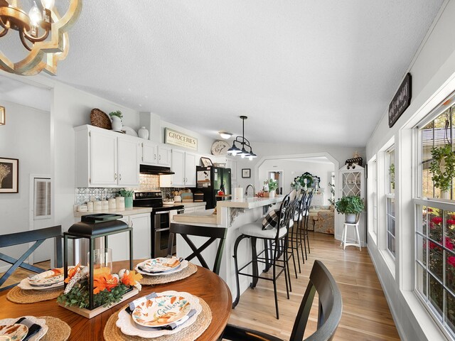 dining room with a textured ceiling, light wood-type flooring, a chandelier, and lofted ceiling