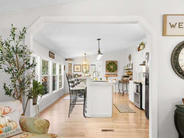 kitchen featuring a breakfast bar, white cabinets, vaulted ceiling, and light wood-type flooring