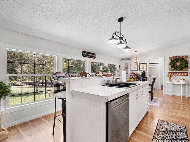 kitchen featuring white cabinets, an island with sink, sink, stainless steel dishwasher, and decorative light fixtures