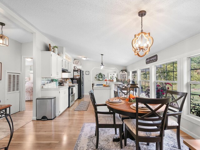 dining area featuring ceiling fan with notable chandelier, a textured ceiling, light wood-type flooring, and vaulted ceiling