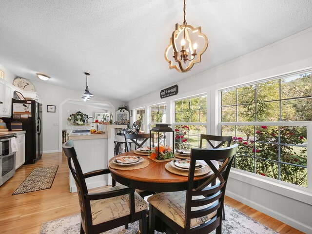 dining space featuring an inviting chandelier, light hardwood / wood-style flooring, a textured ceiling, and lofted ceiling