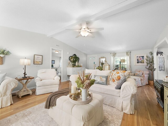 living room featuring ceiling fan, a textured ceiling, light wood-type flooring, and lofted ceiling with beams