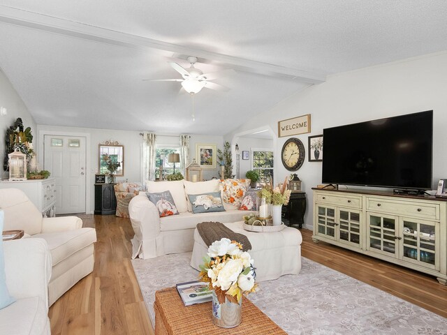 living room with a textured ceiling, vaulted ceiling with beams, ceiling fan, and light hardwood / wood-style flooring