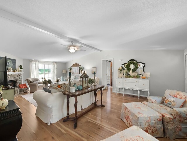 living room with lofted ceiling with beams, a fireplace, a textured ceiling, ceiling fan, and light hardwood / wood-style flooring