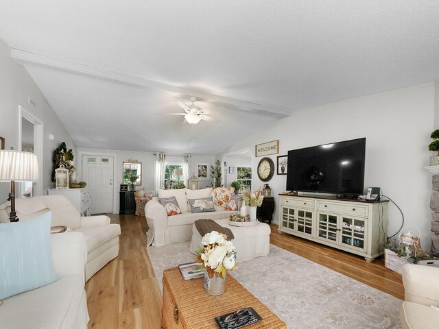 living room featuring vaulted ceiling with beams, light hardwood / wood-style floors, ceiling fan, and a textured ceiling