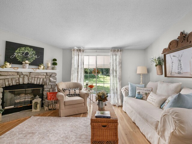 living room featuring a textured ceiling, a stone fireplace, and light hardwood / wood-style flooring