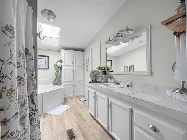 bathroom with vanity, vaulted ceiling with skylight, a textured ceiling, a bathing tub, and hardwood / wood-style flooring