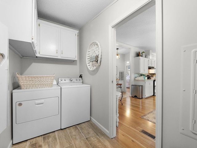 laundry room with cabinets, a textured ceiling, light hardwood / wood-style floors, and washer and dryer