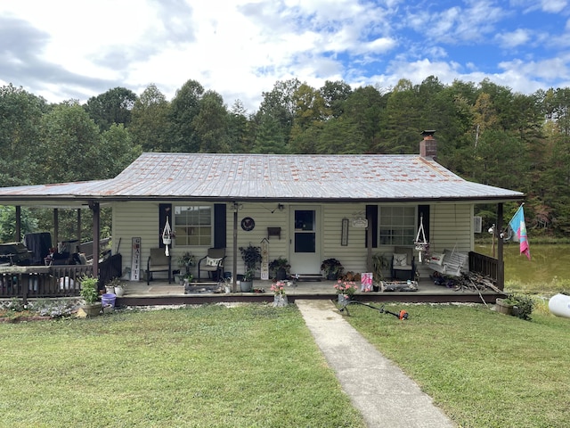 view of front of house with a chimney, covered porch, a front lawn, and metal roof