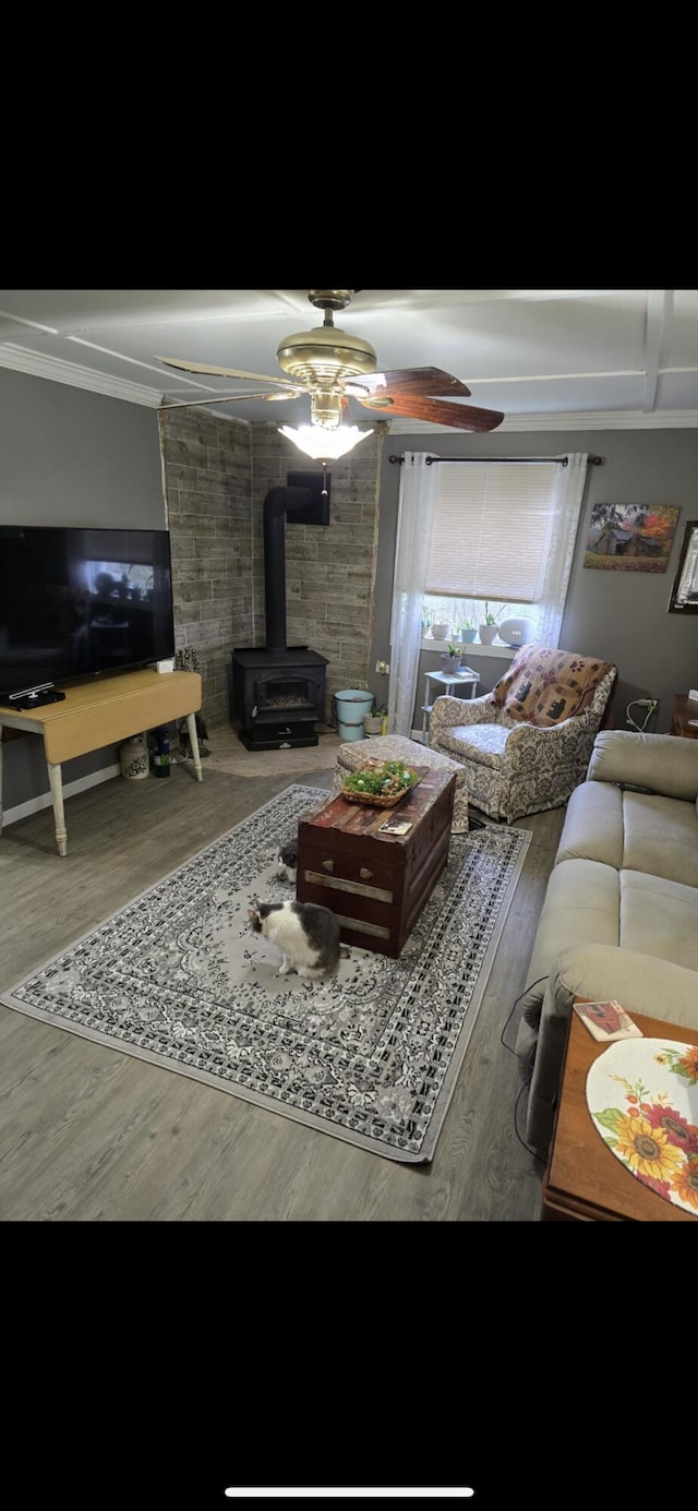 living area featuring crown molding, a wood stove, a ceiling fan, and wood finished floors