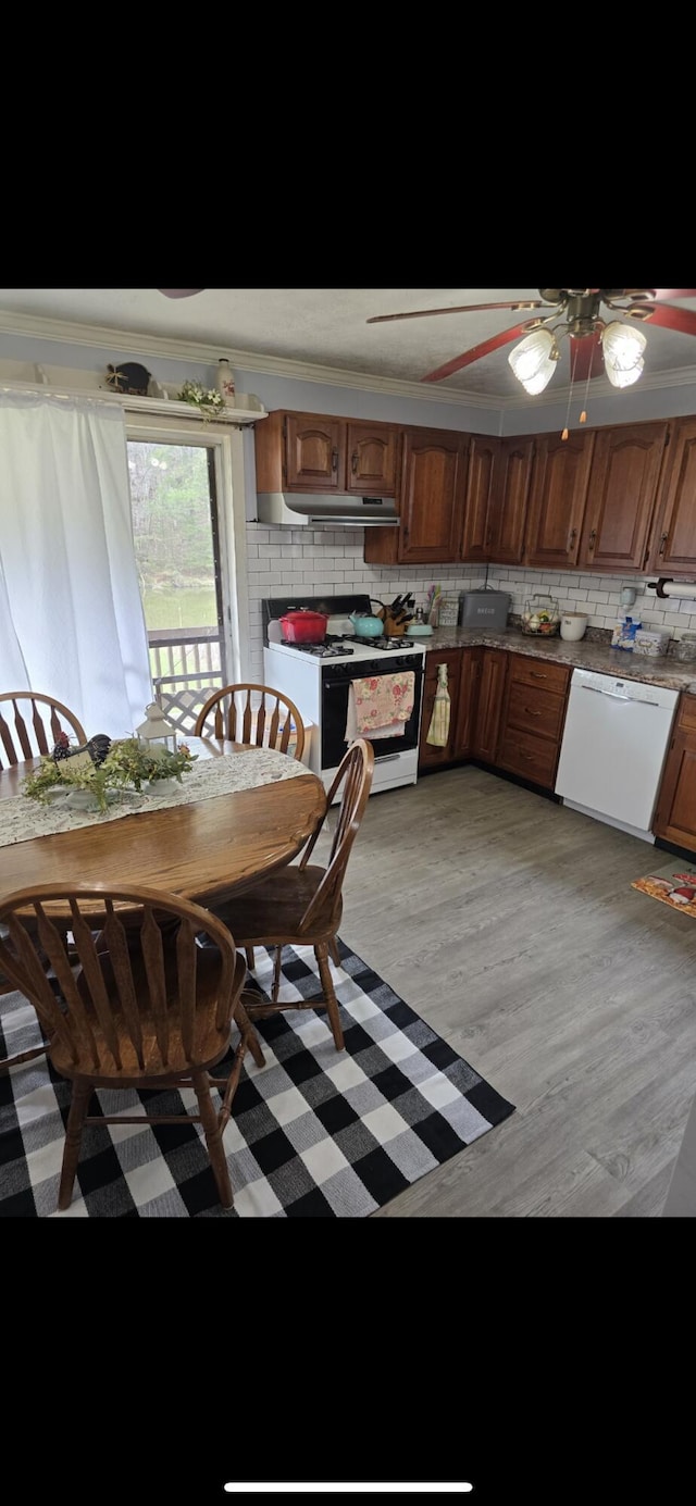 kitchen with white appliances, a ceiling fan, under cabinet range hood, light wood finished floors, and decorative backsplash