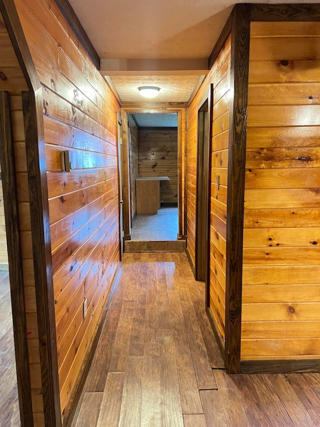 hall featuring a textured ceiling, wood walls, and dark hardwood / wood-style flooring