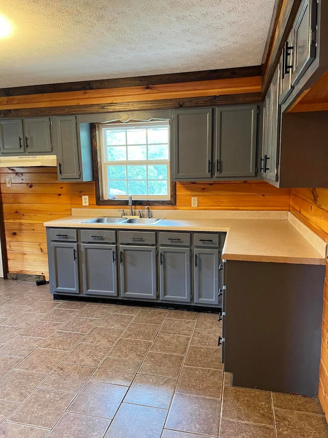 kitchen featuring a textured ceiling, wood walls, sink, and dark tile patterned flooring