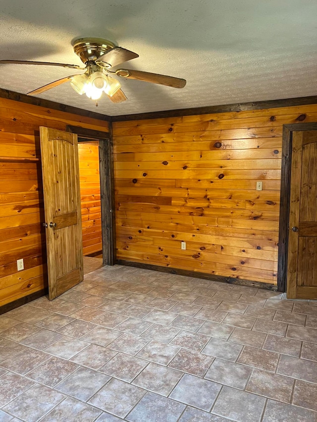 unfurnished bedroom featuring wooden walls, ceiling fan, and a textured ceiling