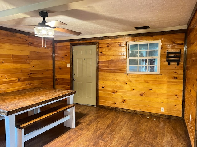 unfurnished dining area with ceiling fan, a textured ceiling, wood walls, and dark hardwood / wood-style flooring