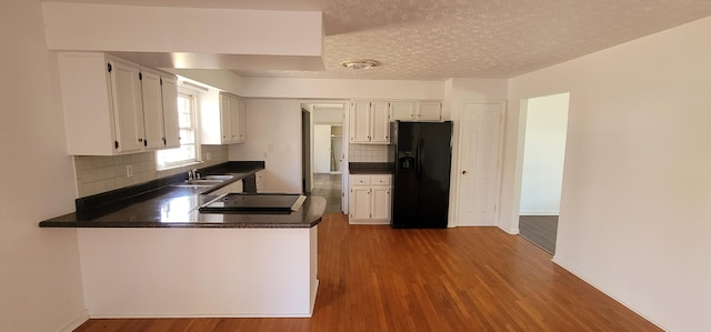 kitchen with kitchen peninsula, a textured ceiling, white cabinetry, and black fridge