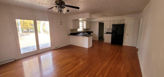 kitchen featuring dark wood-type flooring, black fridge, a textured ceiling, decorative backsplash, and white cabinets