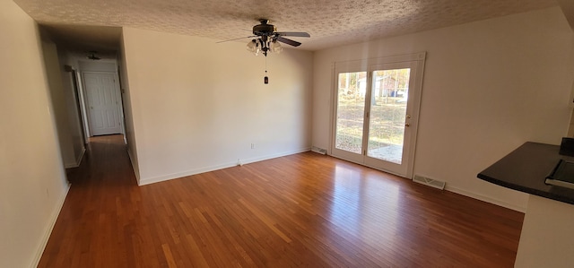 unfurnished living room featuring a textured ceiling, ceiling fan, and dark wood-type flooring