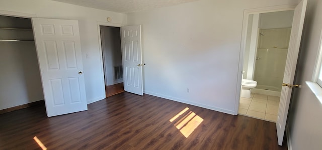 unfurnished bedroom featuring dark hardwood / wood-style flooring, a textured ceiling, connected bathroom, and a closet