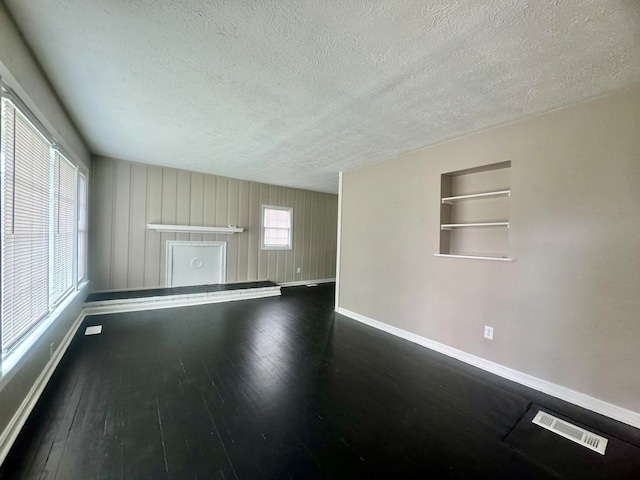 empty room with built in shelves, a textured ceiling, and dark hardwood / wood-style floors