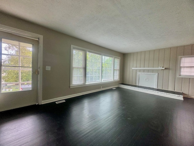 unfurnished living room featuring a textured ceiling, a fireplace, dark hardwood / wood-style floors, and a wealth of natural light