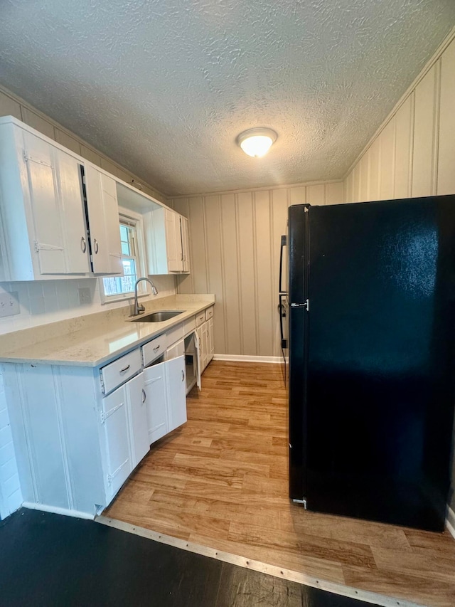 kitchen with a textured ceiling, black fridge, sink, white cabinets, and light hardwood / wood-style flooring