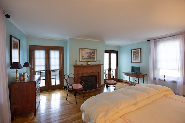 bedroom with a brick fireplace, multiple windows, wood-type flooring, and french doors