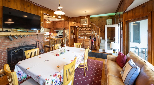 dining space featuring light wood-type flooring, a fireplace, wooden walls, crown molding, and ceiling fan