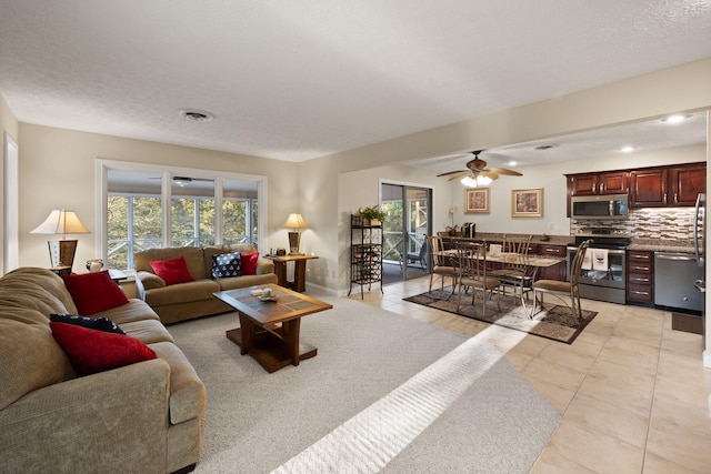 living room with ceiling fan, light tile patterned flooring, a textured ceiling, and a wealth of natural light