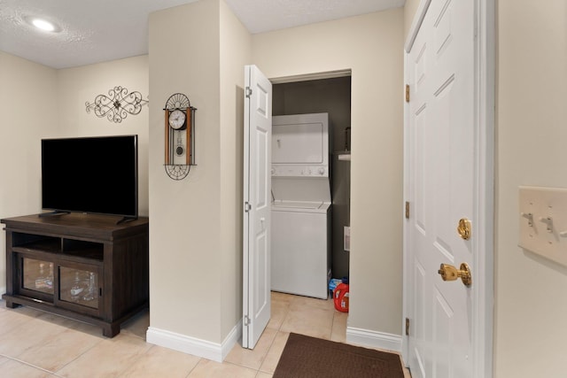 hallway featuring a textured ceiling, light tile patterned flooring, and stacked washer and dryer