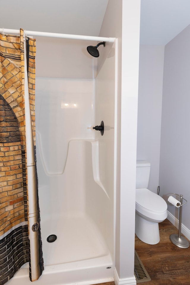 bathroom featuring walk in shower, wood-type flooring, brick wall, and toilet