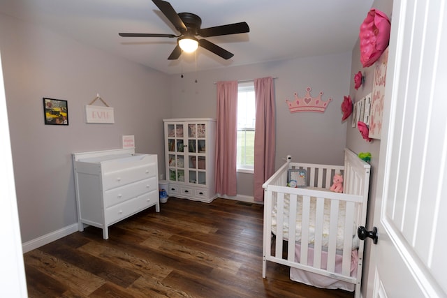 bedroom with dark wood-type flooring, ceiling fan, and a nursery area