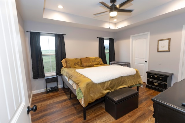 bedroom with ceiling fan, multiple windows, a raised ceiling, and dark hardwood / wood-style flooring