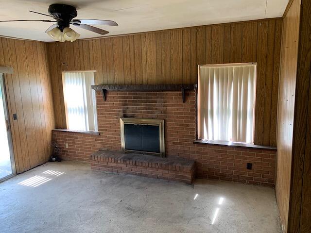 unfurnished living room with ceiling fan, a fireplace, wood walls, and brick wall