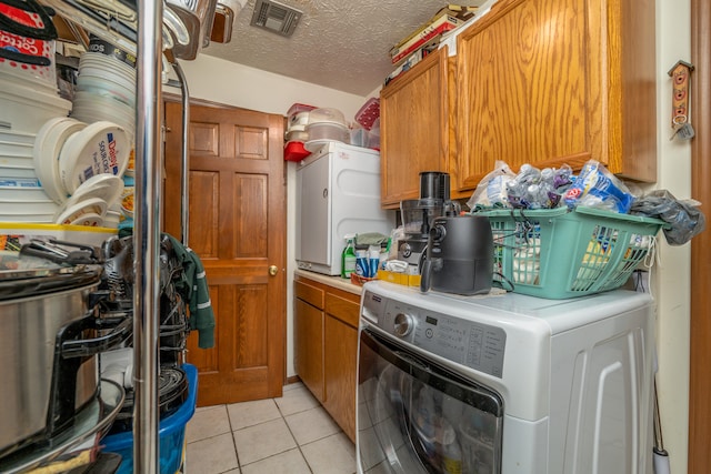 laundry room featuring cabinets, light tile patterned flooring, a textured ceiling, and washer / dryer